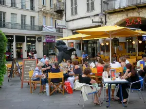 Agen - Place des Laitiers square: café terrace, statue of pilgrim St James de Compostela, shops and facades of houses in the old town