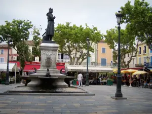 Aigues-Mortes - Place Saint-Louis: St. Louis statua, fontana, lampioni, ristoranti all'aperto, platani (alberi) e facciate di case