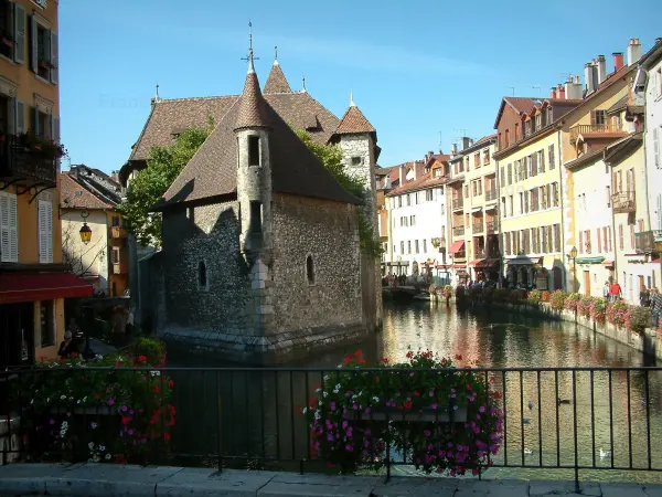 Annecy - Flower-bedecked  bridge with view of the Île palace (former prison) home to the Annecy History museum, Thiou canal and its water birds, Île quayside and houses with colourful facades in the old town