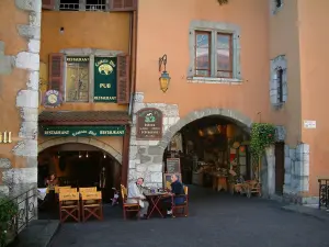 Annecy - Casas con soportales y fachadas de colores, una terraza de un restaurante y una tienda