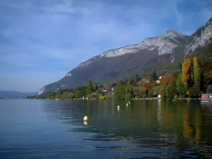 Annecy lake - Lake, yellow buoys, trees with autumn colours, houses, forest and mountain