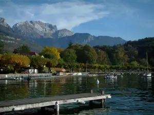 Annecy lake - Wooden pontoon, lake, boats, trees with autumn colours and mountains