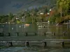 Annecy lake - Lake with wooden pontoons, boat and buoys, houses, trees and forest in autumn