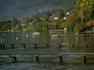 Annecy lake - Lake with wooden pontoons, boat and buoys, houses, trees and forest in autumn