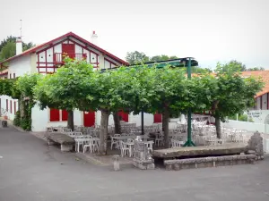 Arcangues - Casa blanca con los obturadores rojos y sombreada terraza del restaurante con el plano