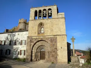 Arlempdes - Romaanse kerk Saint-Pierre met een klokkentoren met vier arcades, stenen kruis versierd met figuren, gevel van een huis in het dorp en overblijfselen van het middeleeuwse kasteel op de achtergrond