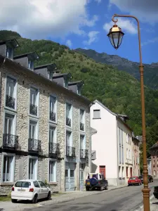 Aulus-les-Bains - Lamppost, street facades of houses in the village (spa town), forest and mountains of Upper Couserans in the background