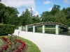 Bagnoles-de-l'Orne - Parterre de fleurs et promenade en premier plan avec vue sur la passerelle fleurie enjambant le lac