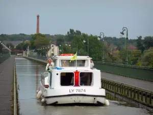 Brug- kanaal van Briare - Boot bewegen op de waterweg van de kanaalbrug, jaagpaden en lantaarnpalen, bomen en huizen op de achtergrond