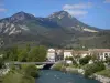 Castellane - Verdon river lined with shrubs and trees, bridge, houses of the old town and mountains; in the Verdon Regional Nature Park