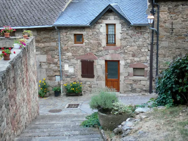 Castelnau-Pégayrols - Fachada de una casa de piedra y adornos florales de la villa medieval