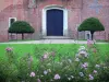 Castillo de Rambures - La entrada de la fortaleza feudal (castillo) llena de arbustos podados, césped y flores en primer plano