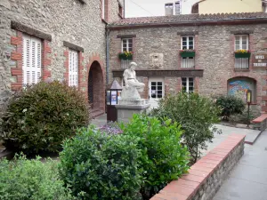 Céret - Fassade der Touristeninformation von Céret und Standbild der sitzenden Catalane umgeben von Blumen und Sträuchern
