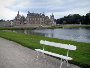 Château de Chantilly - Parc : jardin à la française de Le Nôtre : banc en premier plan, la Manche, pelouses et château