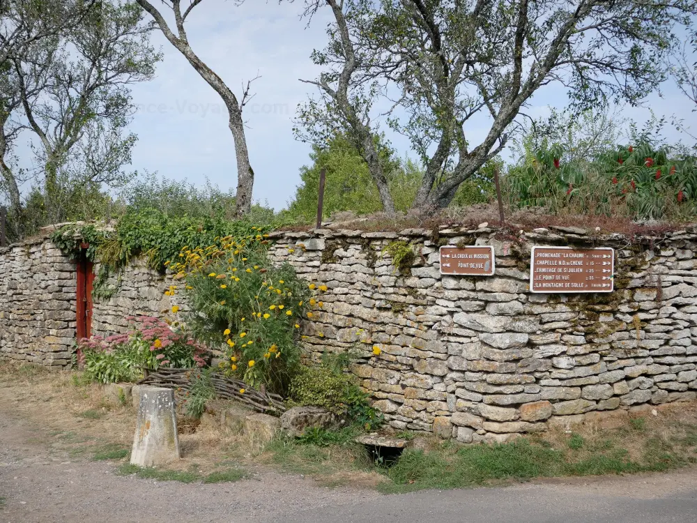 Châteauneuf-en-Auxois - Châteauneuf: Mur en pierre orné de fleurs avec panneaux directionnels