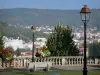 Clermont-Ferrand - Grünanlage geschmückt mit einer Bank, Laternen und Blumen mit Blick auf die Bäume und Gebäude der Stadt