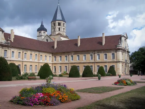 Cluny abbey - Benedictine abbey: the Eau Bénite bell tower and the Clock tower (remains of the Saint-Pierre-et-Saint-Paul abbey church), convent buildings, garden featuring flowerbeds and cut shrubs; heavy sky