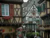 Colmar - Maisons à pans de bois avec des fleurs (géraniums) et de jolies enseignes en fer forgé