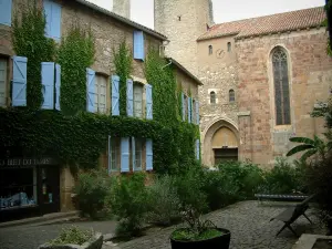 Cordes-sur-Ciel - Square decorated with benches and shrubs, stone house covered with ivy and with blue shutters, Saint-Michel church