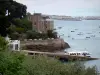 Dinard - Station balnéaire de la côte d'Émeraude : promenade du Clair de Lune, bateau amarré à l'embarcadère, maisons, mer avec des bateaux et en arrière-plan la ville close (cité corsaire) de Saint-Malo et son port 