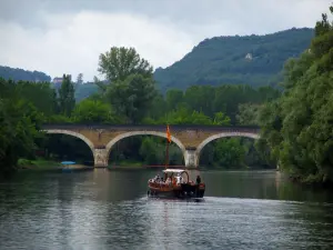 Dordogne valley - Navigating gabarre, bridge spanning the River Dordogne, trees along the water, forest and hill, in Périgord