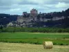 Dordogne valley - Straw bale in foreground and fields with view of the village of Beynac-et-Cazenac, its castle, its cliff and its houses, cloudy sky, in Périgord