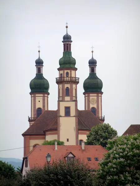 Ebersmunster - Abteikirche mit drei Zwiebeltürmen, Dach eines Hauses und Bäume