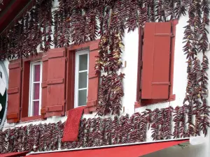 Espelette - Gevel van een huis met rode luiken versierd met slingers van paprika
