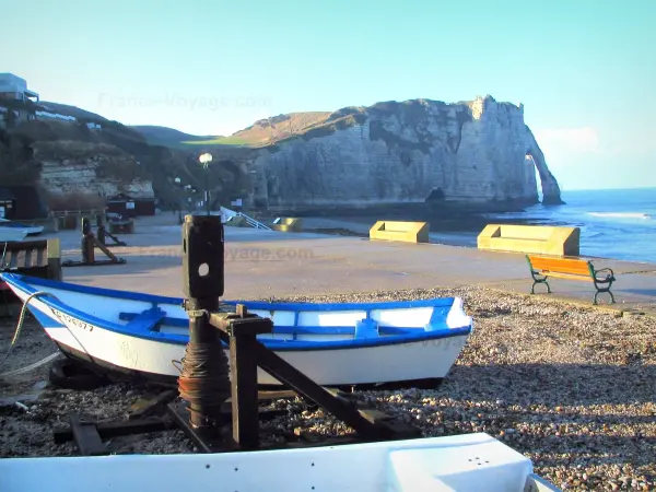 Étretat - Boats, pebbles, promenade of the seaside resort, bench, the Aval cliff (chalk cliff) with its arc (the Aval gateway), and the Channel (sea)