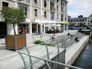 Évreux - Promenade au bord d'un bras de la rivière Iton, arbre en pot, terrasse de café et façades d'immeubles de la ville