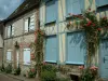 Gerberoy - Maison à pans de bois aux volets bleus avec des rosiers grimpants (roses rouges) et demeure en brique et pierre aux volets blancs