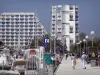 La Grande-Motte - Station balnéaire : quai avec des promeneurs, immeubles, bateaux et voiliers du port de plaisance