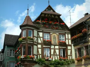 Kaysersberg - Maison fleurie (géraniums) à colombages avec un oriel et un balcon de bois