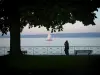 Lac Léman - Arbre, couple, bancs et rambarde dans l'ombre avec vue sur le lac Léman, un voilier et la rive suisse en arrière-plan