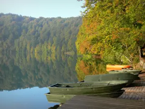 Lac Pavin - Barques au bord du lac et arbres (forêt) aux couleurs d'automne se reflétant dans les eaux ; dans le Parc Naturel Régional des Volcans d'Auvergne, dans le massif du Sancy (monts Dore), près de Besse-et-Saint-Anastaise