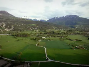 Landscapes of the Hautes-Alpes - Durance valley: prairies, fields, road, Durance river lined with trees and snowy mountain tops (snow)