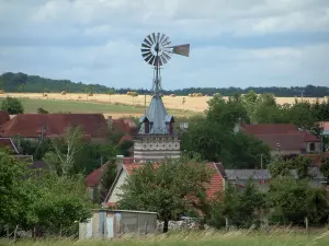 Landschaften der Aube - Windrad, Bäume und Häuser eines Dorfes, Felder mit Strohballen im Hintergrund