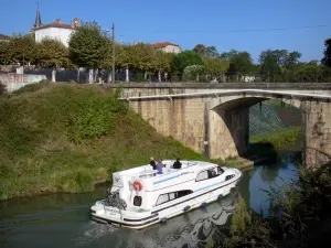 Landschappen van de Berry - Brug over het Canal de Garonne (Canal de Garonne), boot varen op het kanaal, bomen, huizen, en de kerk toren met uitzicht op het geheel van Daman