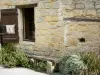 Larressingle - Facade of a stone house, bench and plants 