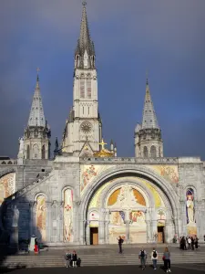 Lourdes - Domaine de la Grotte (sanctuaires, cité religieuse) : escaliers de l'esplanade du Rosaire, portail de la basilique Notre-Dame du Rosaire de style néo-byzantin ; tourelles et clocher de la basilique de l'Immaculée Conception (basilique supérieure) de style néogothique