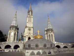 Lourdes - Domaine de la Grotte (sanctuaires, cité religieuse) : coupole de la basilique Notre-Dame du Rosaire surmontée d'une couronne et d'une croix dorée ; tourelles et clocher de la basilique de l'Immaculée Conception (basilique supérieure) de style néogothique