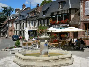 Lyons-la-Fôret - Brunnen geschmückt mit Blumen, Strassencafé und Fassaden von Fachwerkhäusern des Dorfes