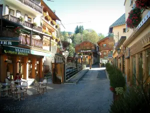 Megève - Cafetería con terraza, pequeño puente sobre el río, tiendas y casas de la aldea (estación de esquí y en verano)