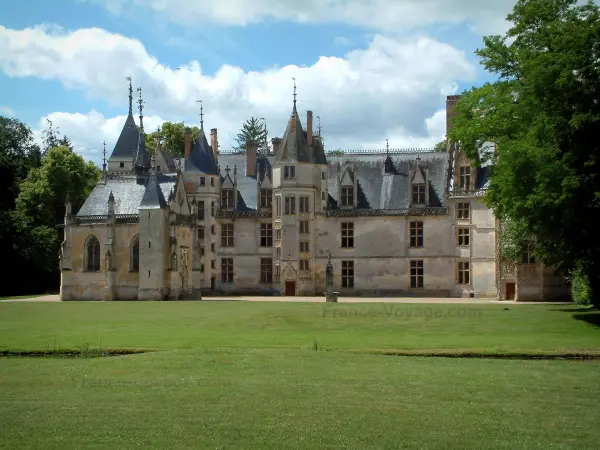 Meillant castle - Park, trees, chapel and facade of the castle of Flamboyant Gothic style, clouds in the blue sky