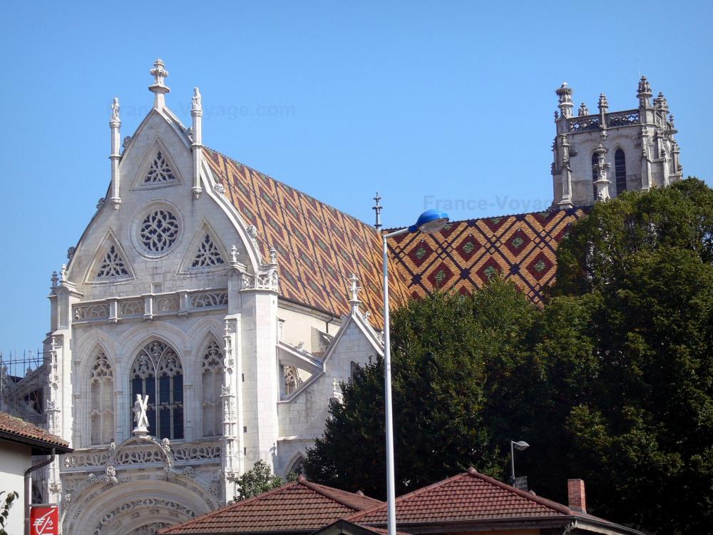 Monastère royal de Brou - Vue sur l'église de Brou avec sa façade sculptée, sa toiture de tuiles vernissées polychromes et son clocher ; sur la commune de Bourg-en-Bresse