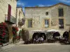 Monpazier - Houses with facades decorated with red climbing roses, arches and café terrace of the Cornières square (central square of the fortified town), in Périgord