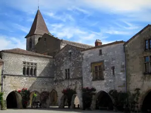 Monpazier - Maisons aux façades ornées de rosiers grimpants et arcades de la place des Cornières (place centrale de la bastide), et clocher de l'église, en Périgord