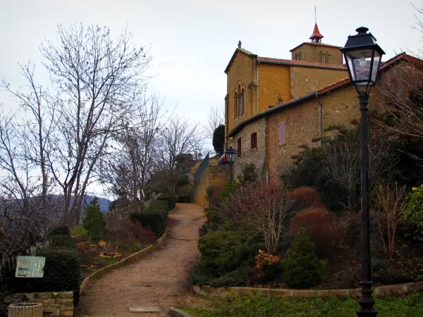 Oingt - Sentier bordé d'arbres et d'arbustes, lampadaire, maison en pierre et église du village médiéval, dans le Pays des Pierres Dorées (Pays Beaujolais)