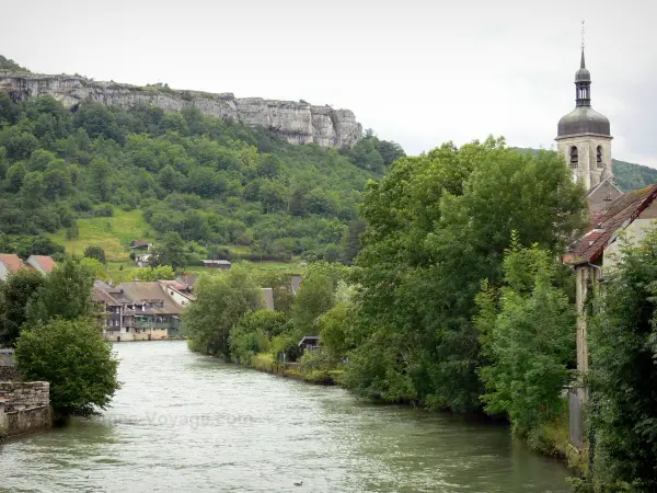 Ornans - Fluss Loue, Bäume und Häuser am Flussufer, Glockenturm der Kirche Saint-Laurent und Felswände (Felsen) im Hintergrund