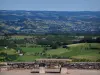 Paesaggi del Quercy - Panchina in pietra si affaccia sui campi, prati, case, alberi e piccole colline